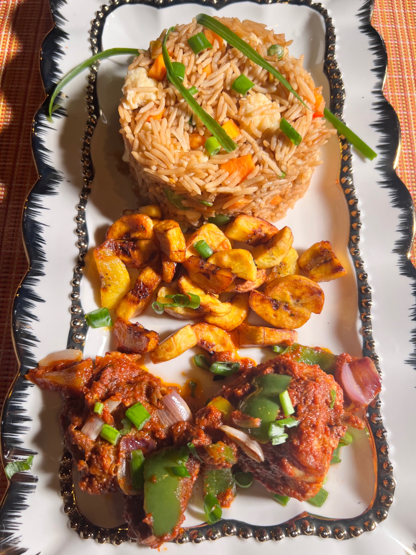 Jollof rice, fried plantain and grilled chicken on a platter