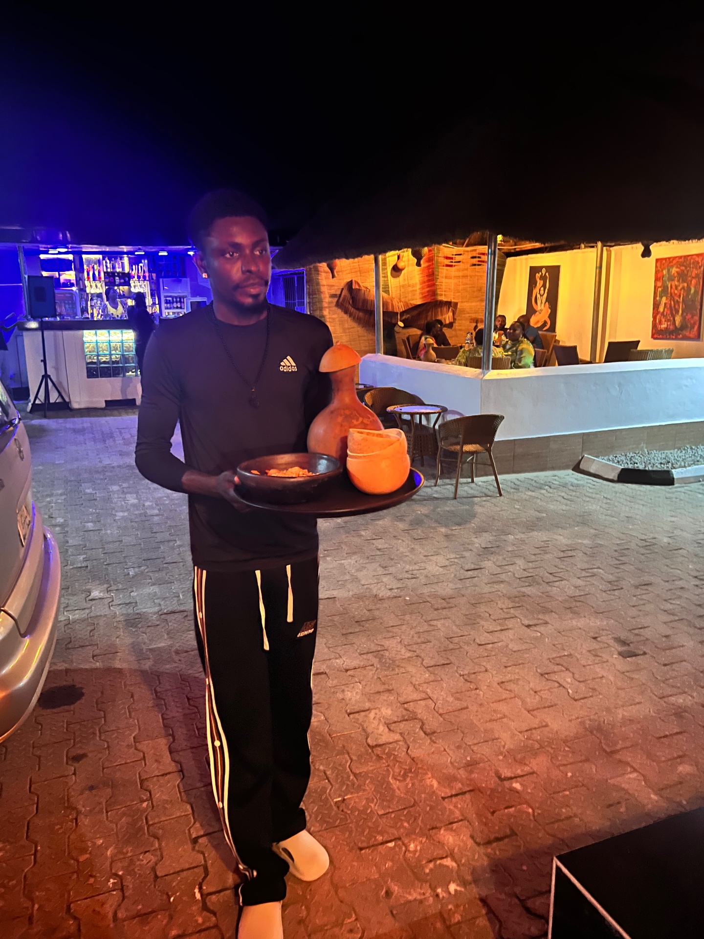 Server carrying a traditional clay serving set at the outdoor bar, evening